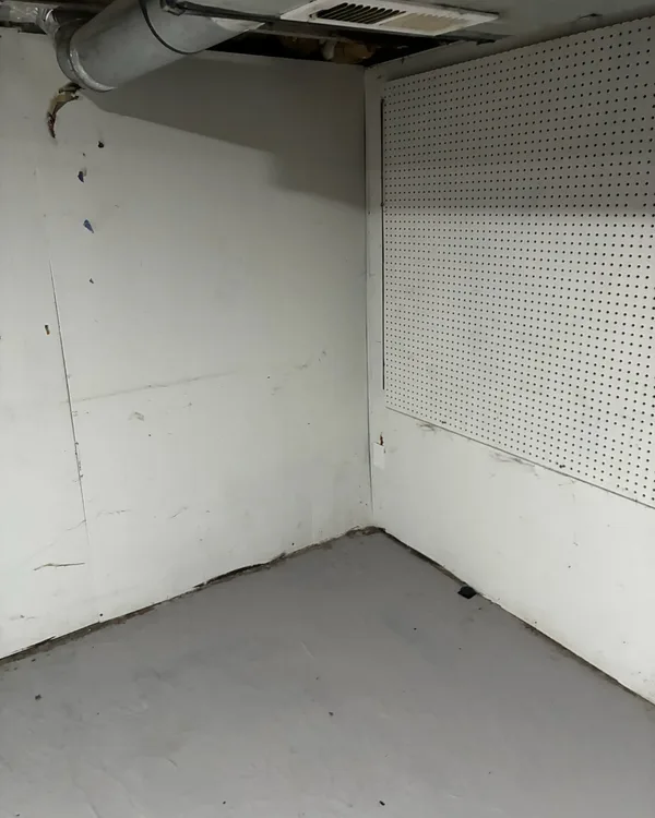 Corner of a basement room with a painted grey floor and a pegboard wall