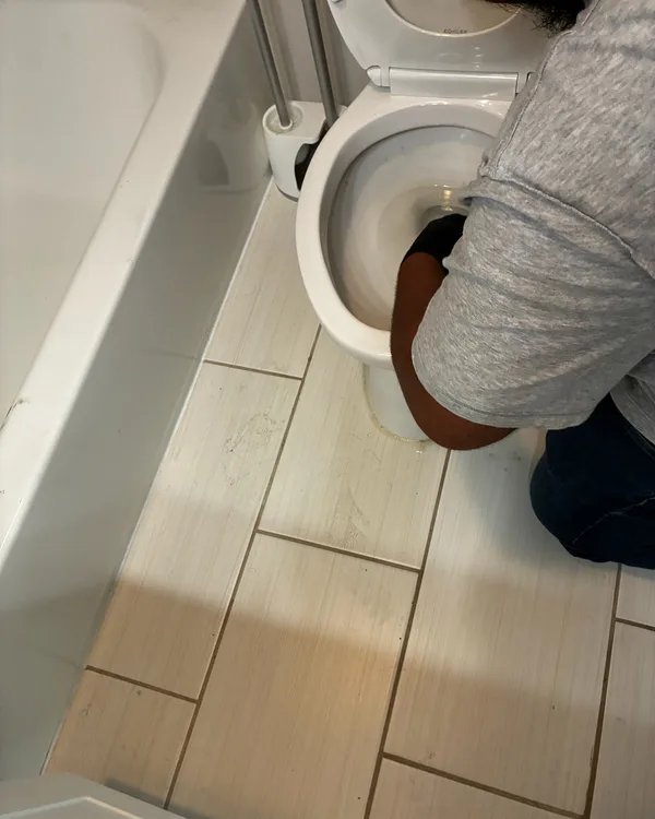 A cleaner scrubbing a toilet next to a bathtub