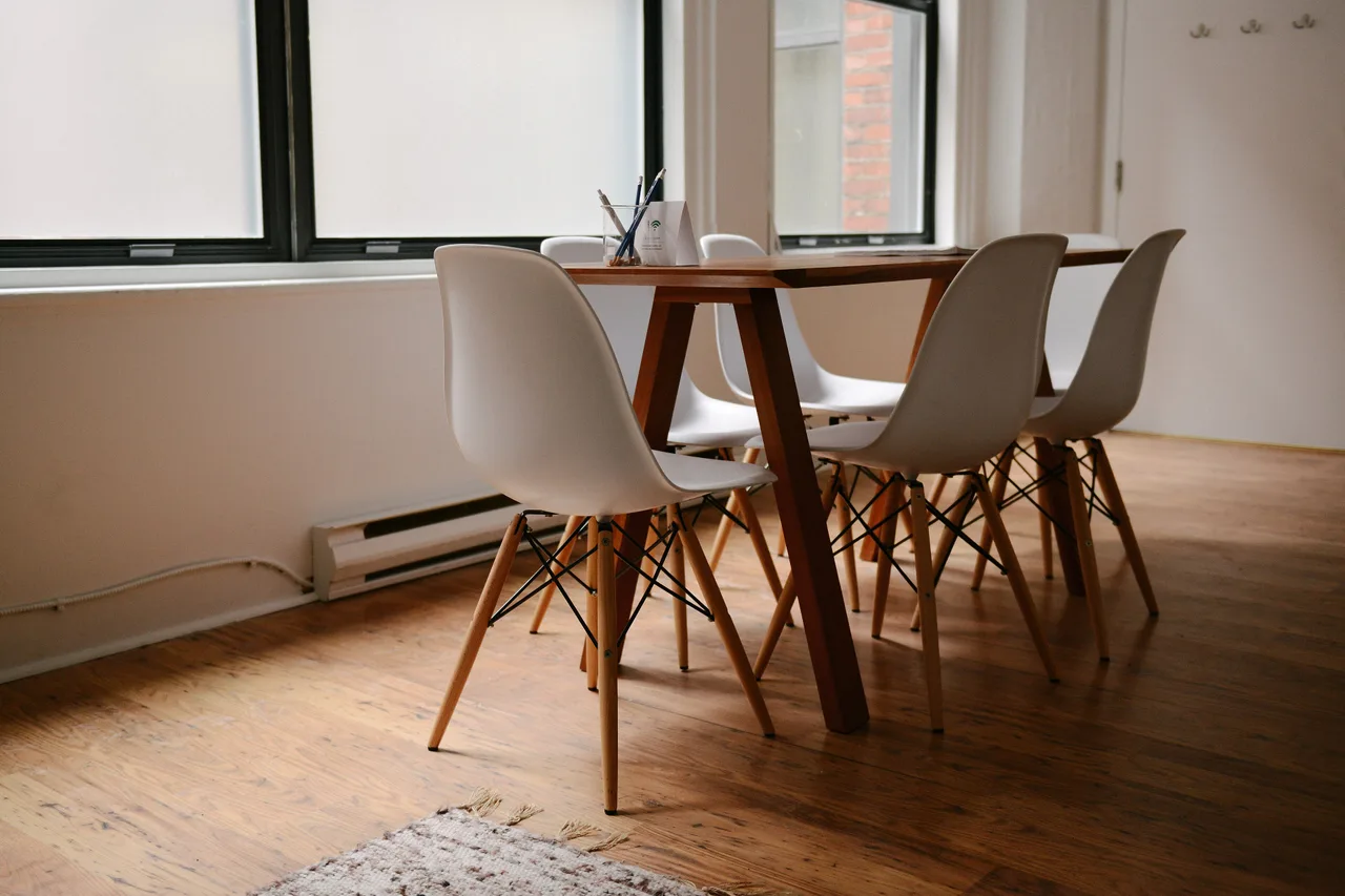A clean, empty meeting room with a wooden table and white chairs